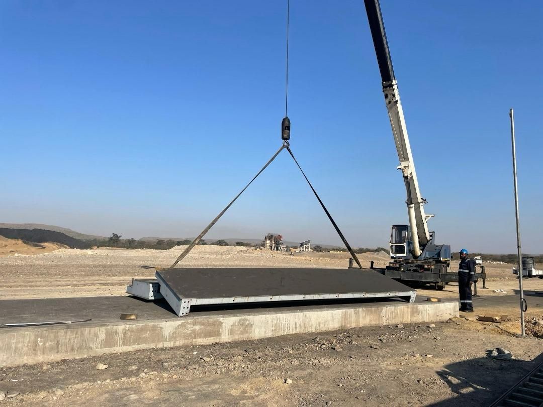 Crane lowering a weighbridge deck section onto its foundation at a mining site